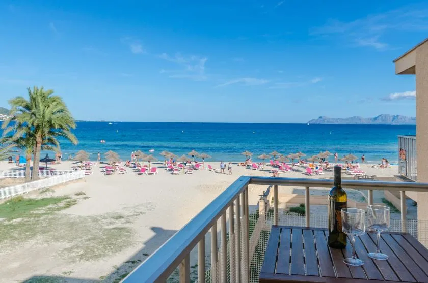 Una terraza frente al mar da a una playa de arena, el mar y filas de sombrillas.