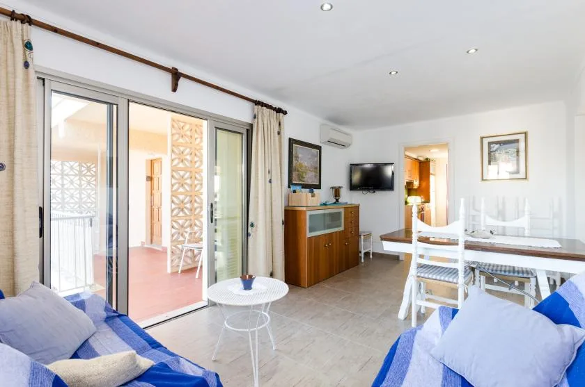 Sala de estar con asientos, un televisor y puertas corredizas de vidrio que dan a un balcón.