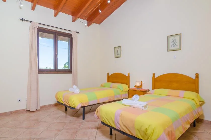 A bedroom with two beds covered in colorful bedding beneath a wooden ceiling.