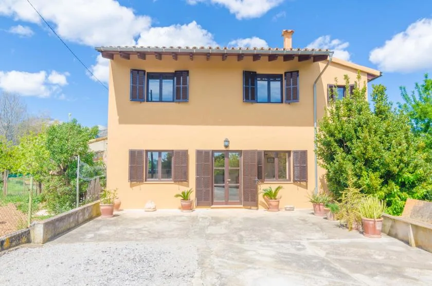 A two-story house with shuttered windows faces a paved courtyard.