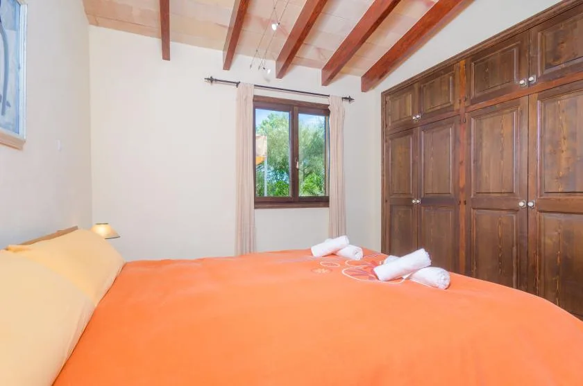 A bedroom with an orange-covered bed, a window, and built-in wooden storage.