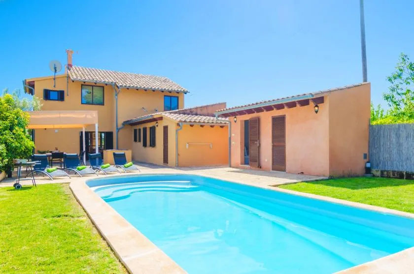 A swimming pool beside a sunny house and green lawn.