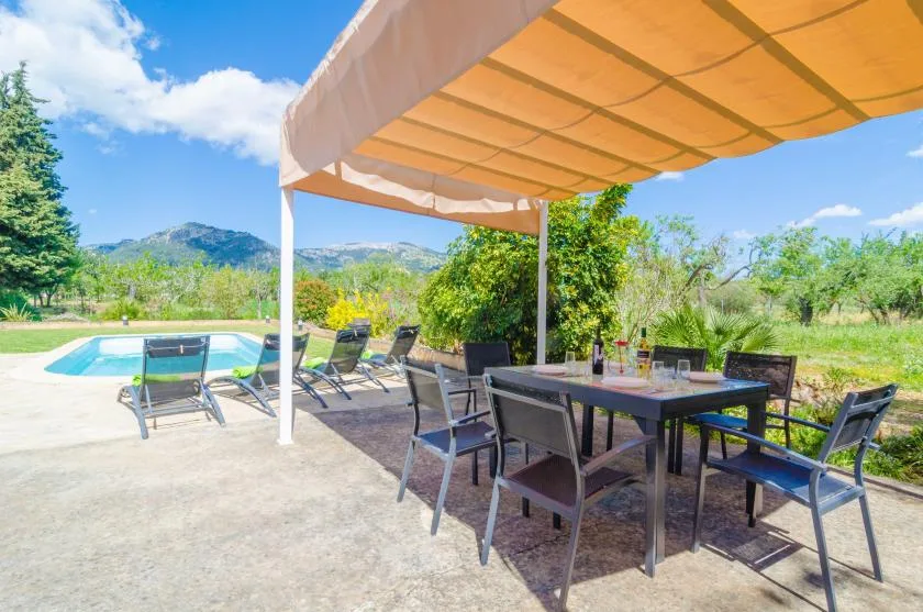 An outdoor dining area under a canopy overlooks a swimming pool and mountain scenery.