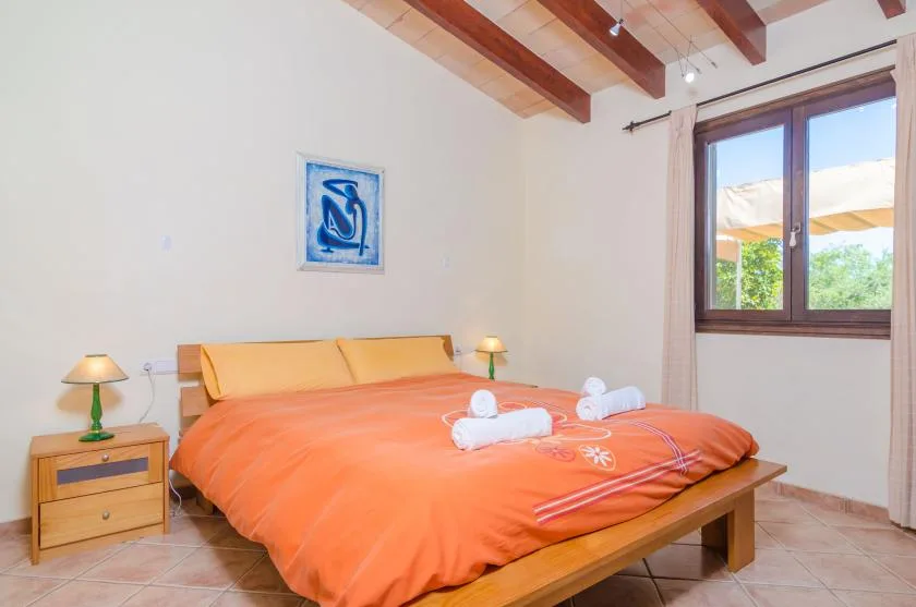 A bedroom with an orange bedspread, bedside tables, and a window.
