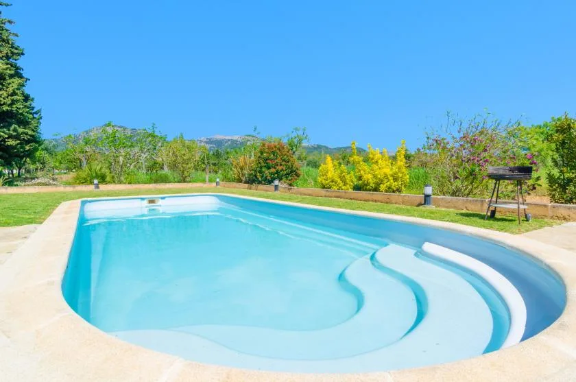 An outdoor swimming pool with curved steps sits among green shrubs.