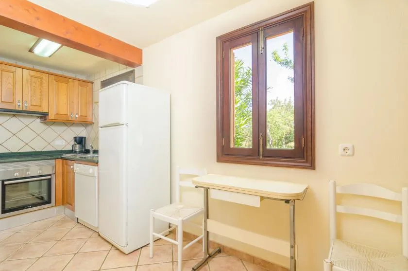 A small kitchen with a refrigerator, counter, and a table beneath a window.