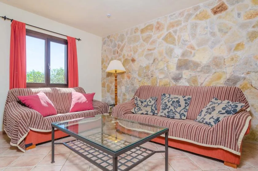 A living room with striped seating, a glass coffee table, and a stone wall.