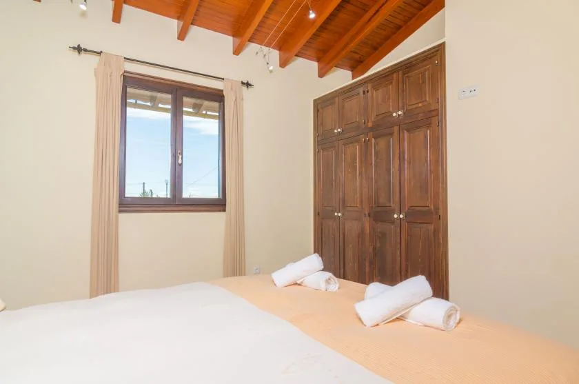 A bedroom with a bed, a window, and a wooden wardrobe beneath a timber ceiling.