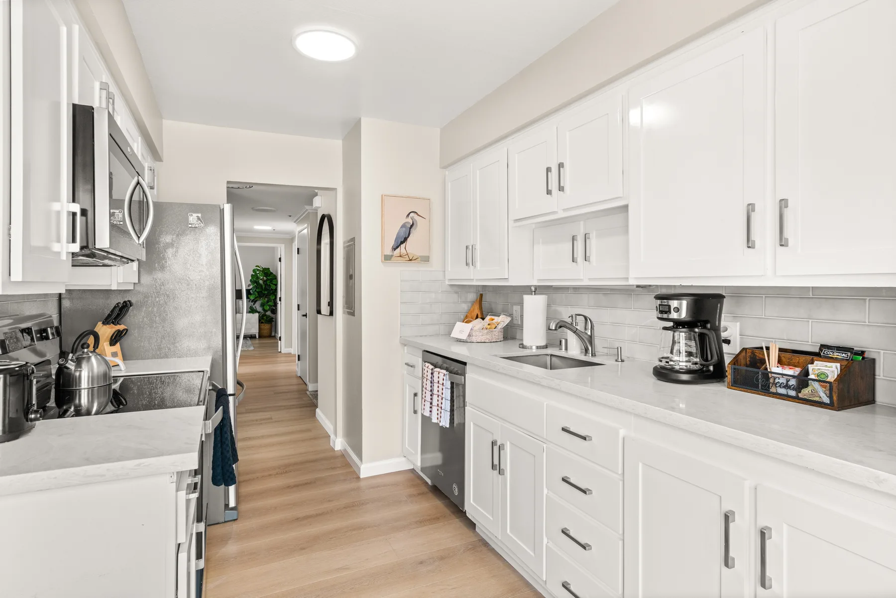 Una cocina luminosa con gabinetes blancos, encimeras claras y electrodomésticos de acero inoxidable.