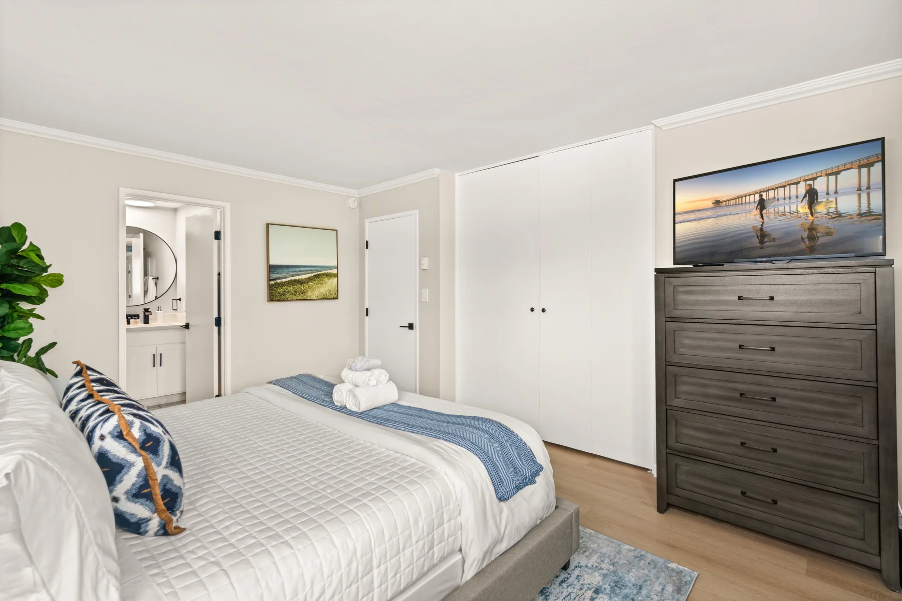 Un dormitorio con una cama bien arreglada y una cómoda con un televisor encima.