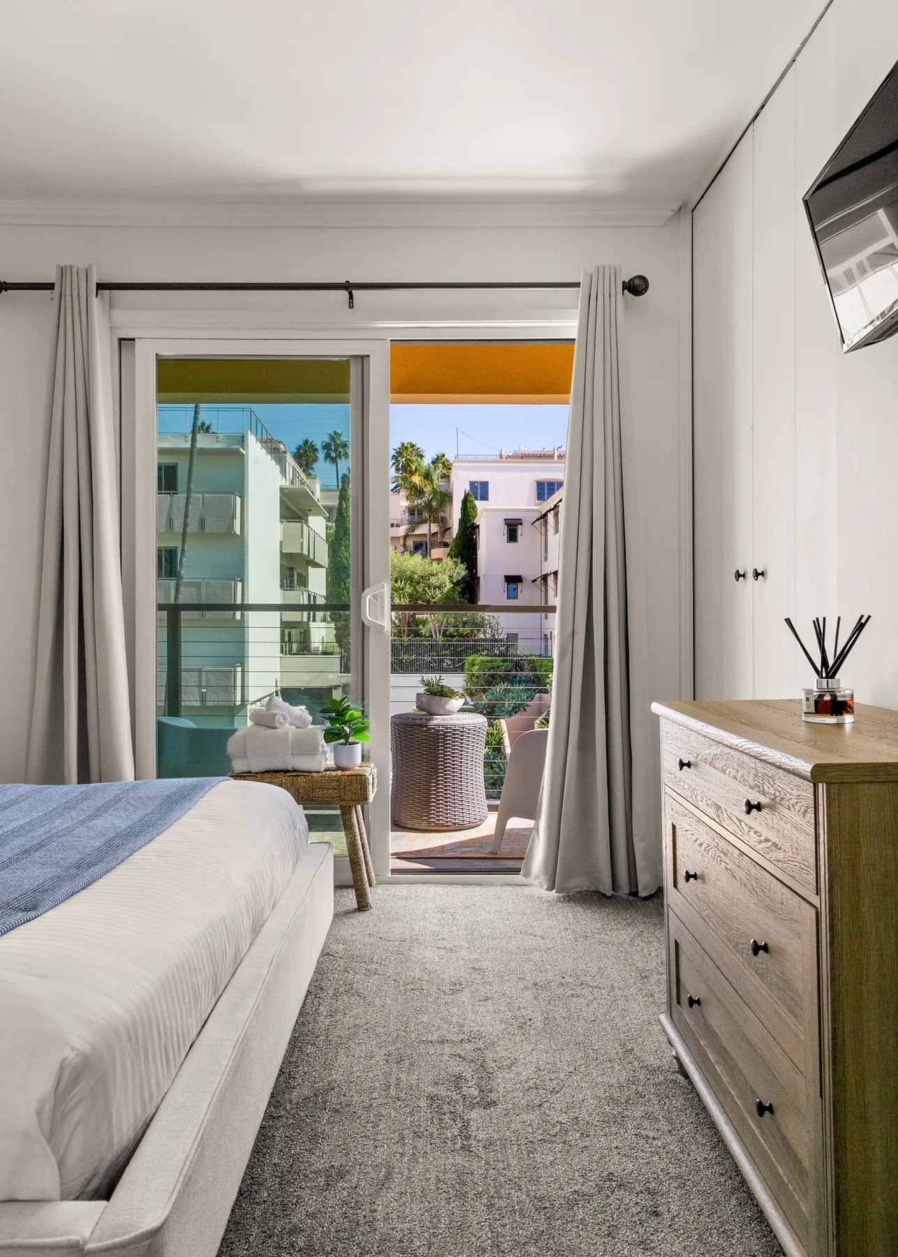 Un dormitorio luminoso con cama, cómoda y puertas corredizas de vidrio que dan a un balcón.