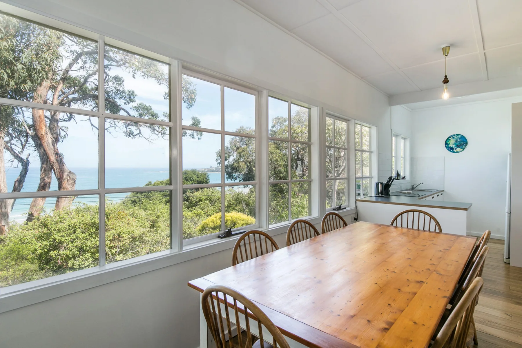 Comedor con una mesa de madera junto a grandes ventanas con vistas al mar.