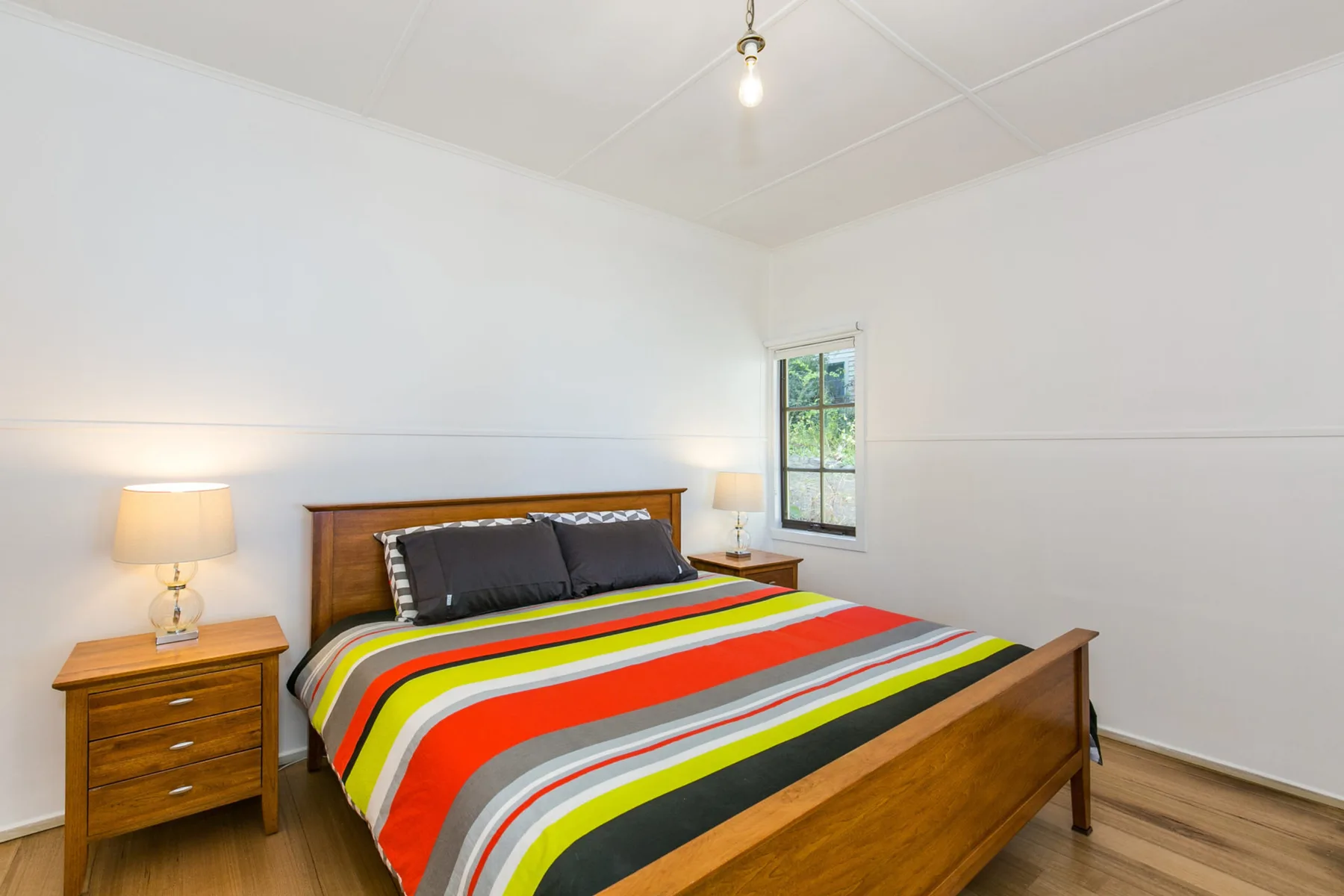 Un dormitorio con una cama de madera cubierta con una colcha de rayas coloridas.