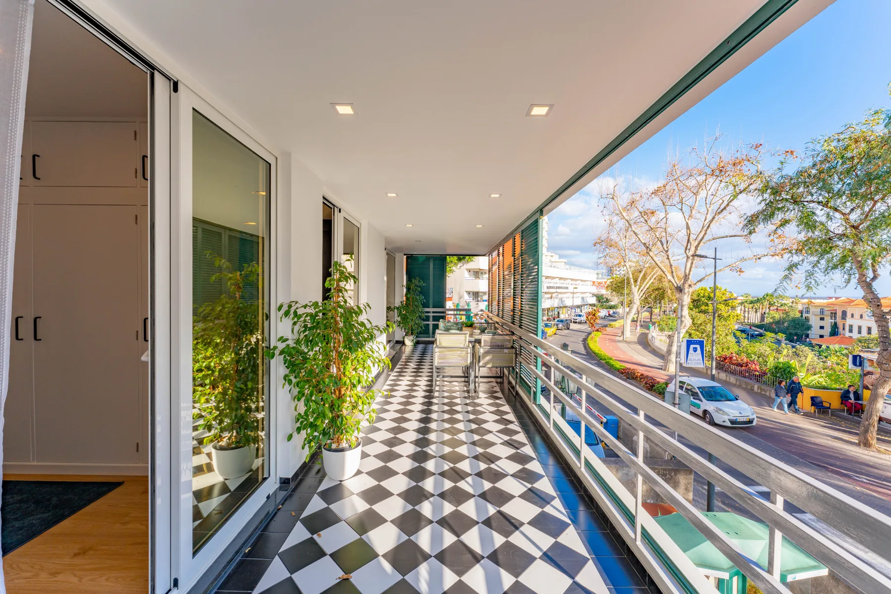 A covered balcony corridor with a patterned floor and railing overlooking a street.