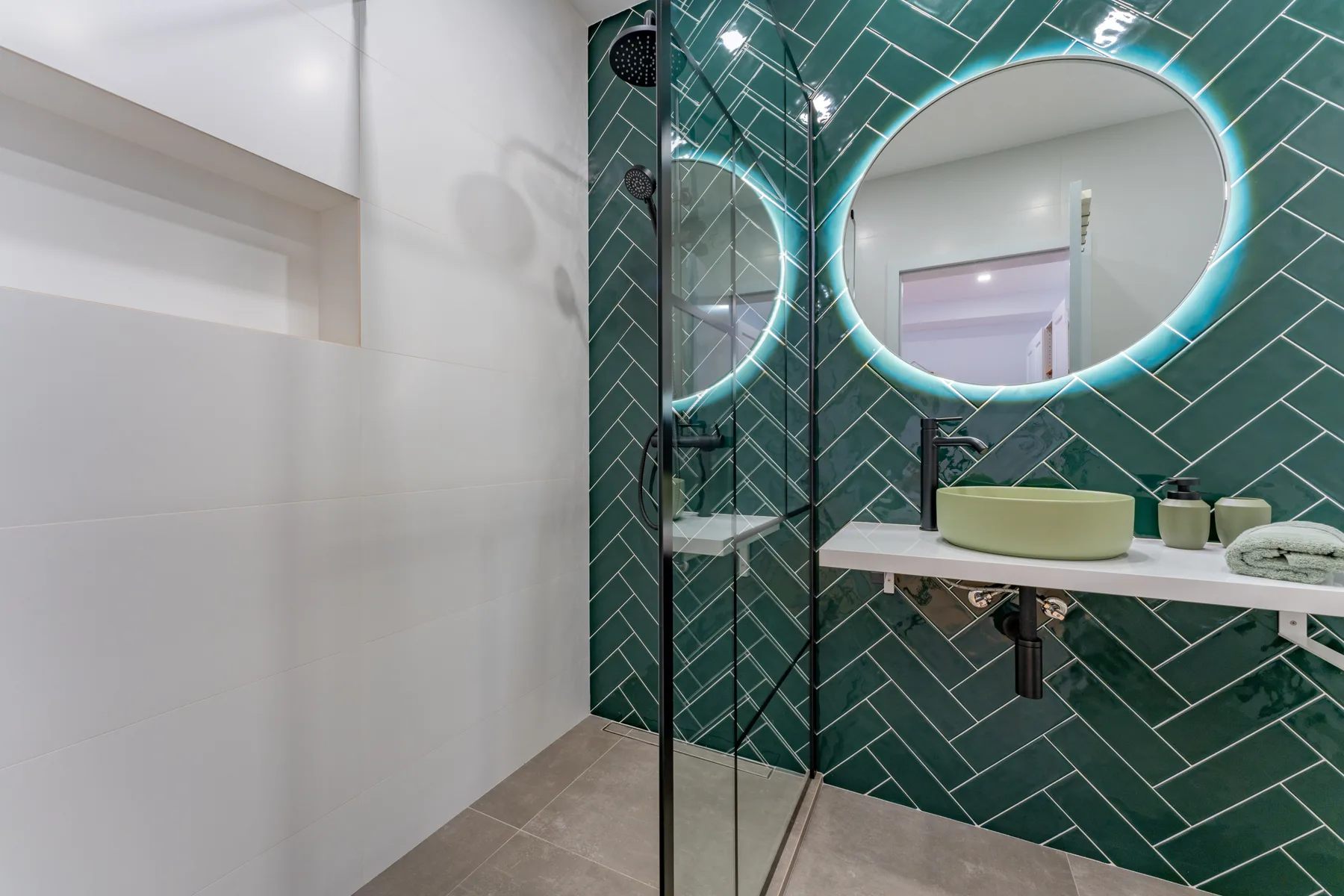 Bathroom with a glass shower and a round illuminated mirror.