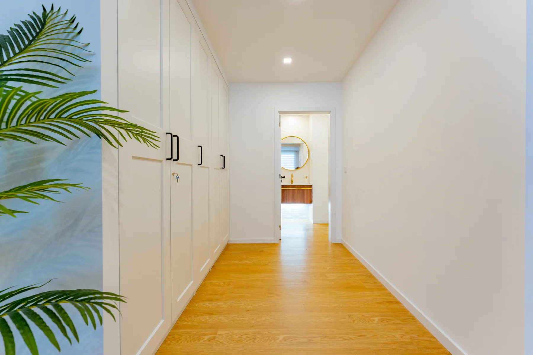 A bright hallway with white built-in cabinets and a wooden floor.