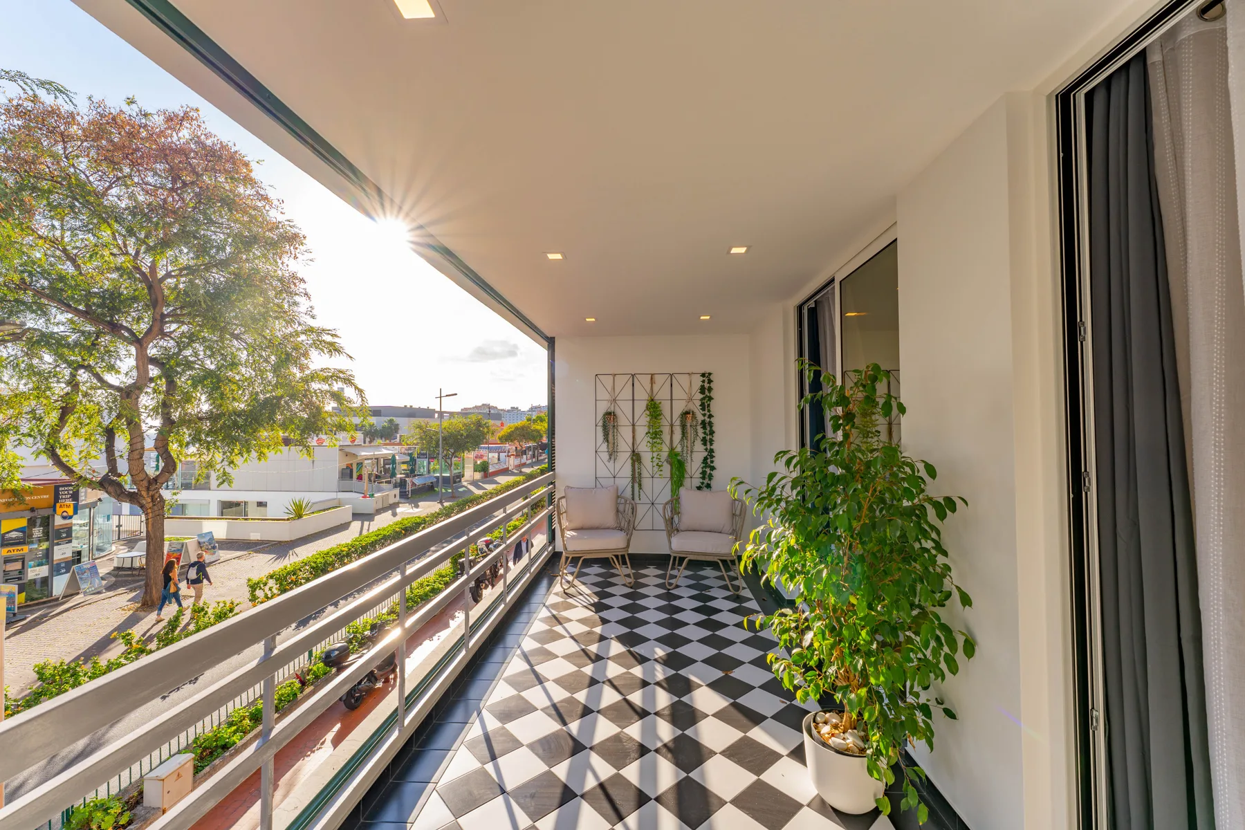 Balcony with patterned tile flooring, potted plants, and a street view.
