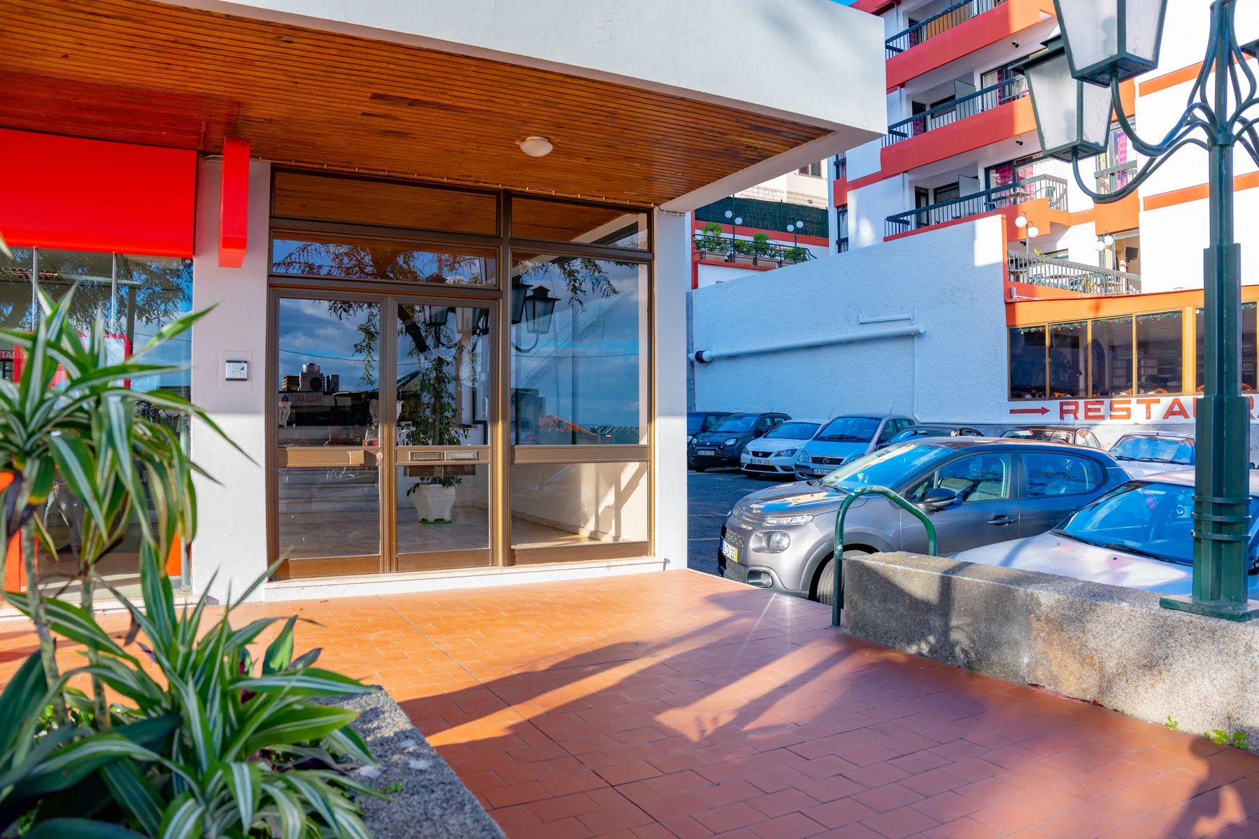A glazed entrance opens onto a tiled walkway beside parked cars.