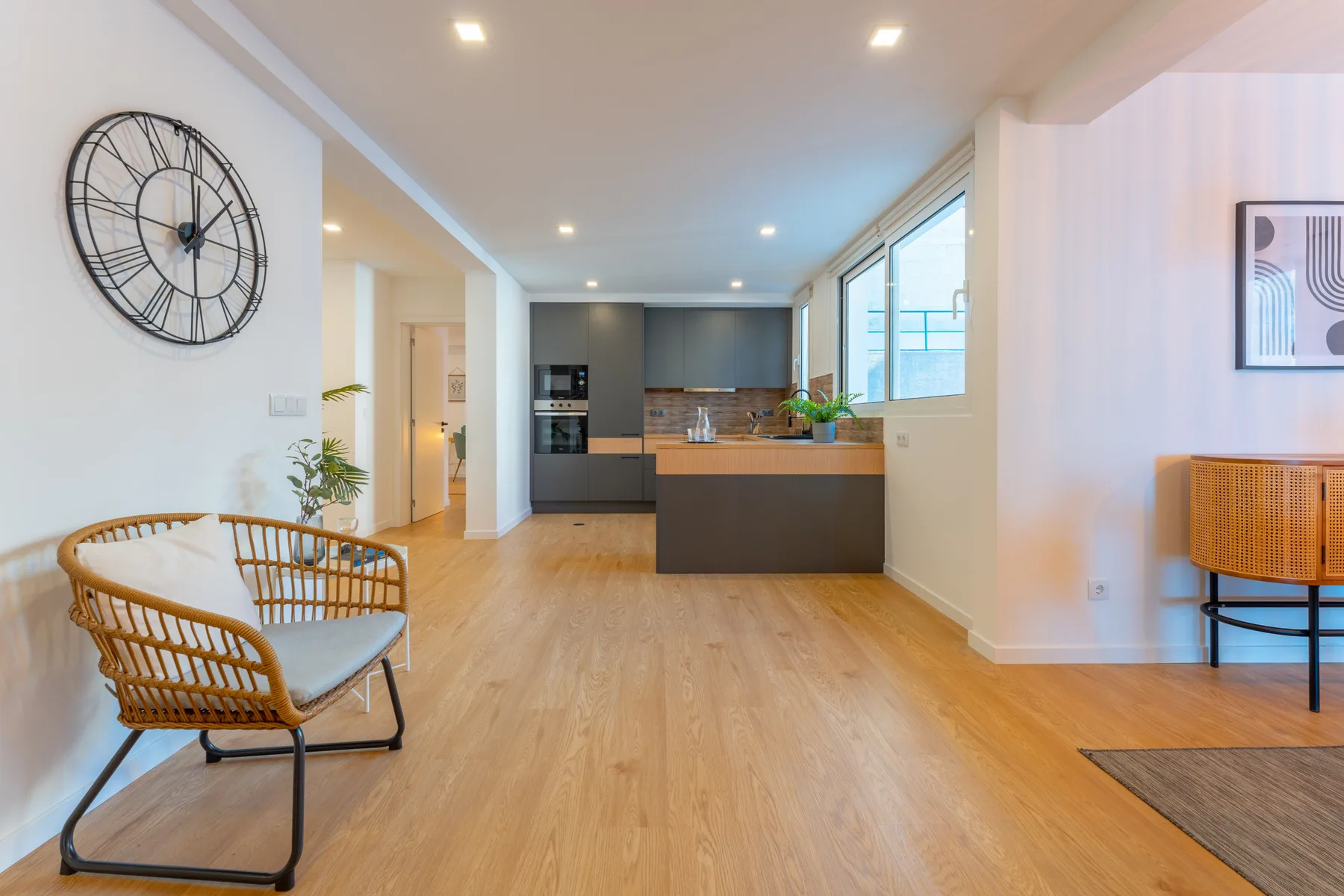A bright open-plan living area with a kitchen and a woven seating chair.