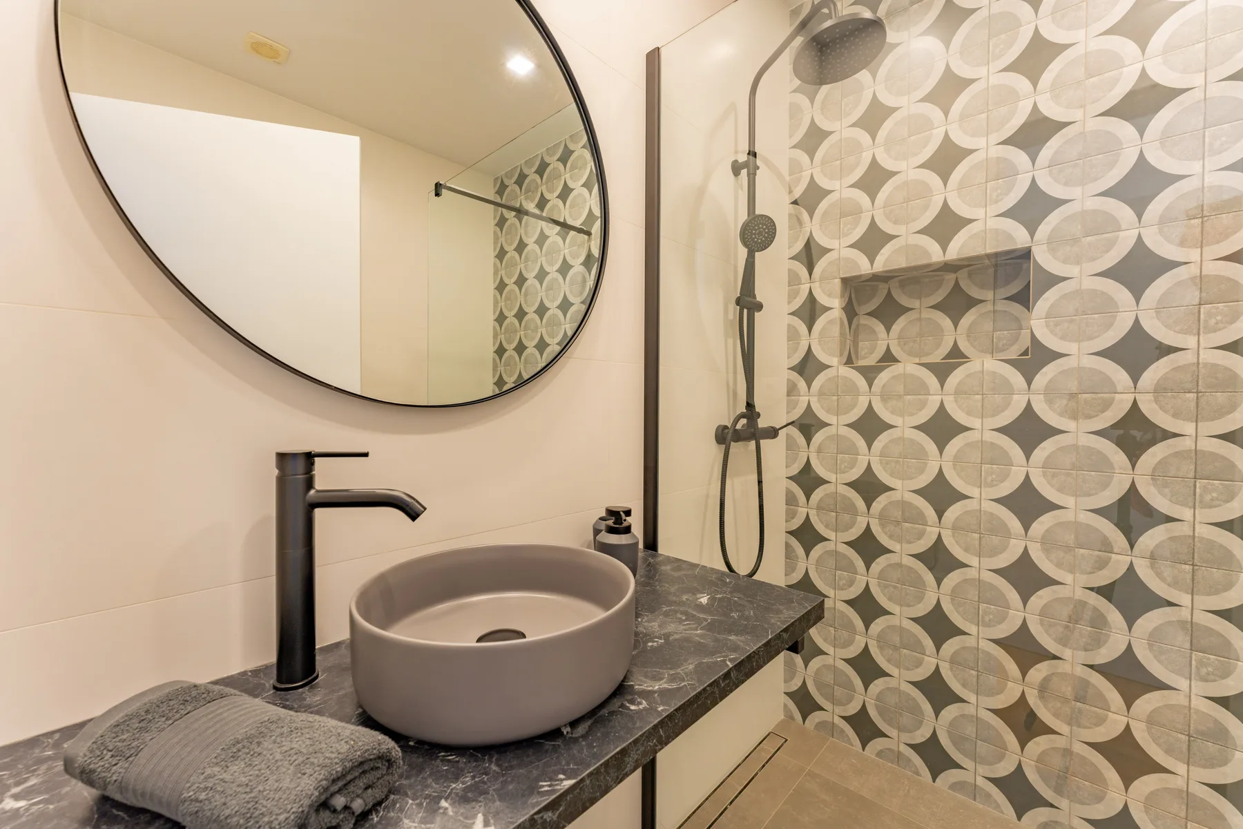 A bathroom vanity with a vessel sink sits beside a patterned shower.