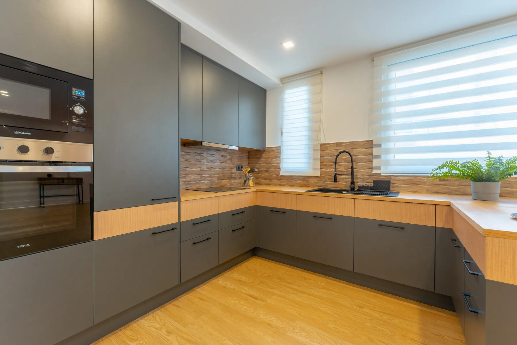 A modern kitchen with gray cabinets, wood-toned counters, and a sink beneath the windows.