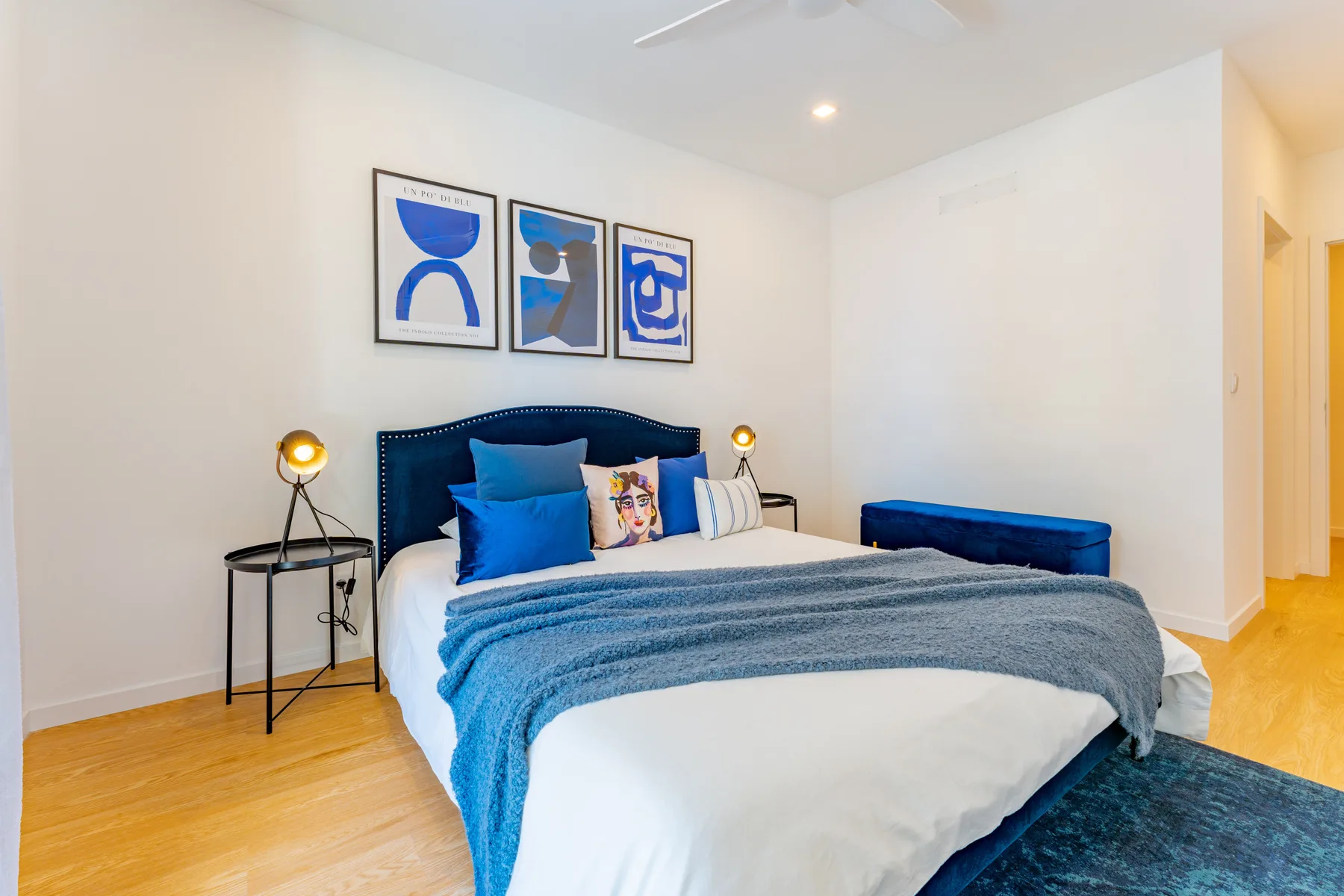 A bedroom with a bed, blue headboard, and framed artwork.