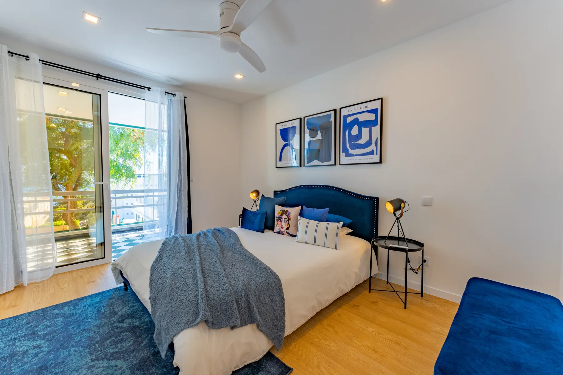 A bedroom with a bed, blue headboard, and glass doors opening onto a balcony.
