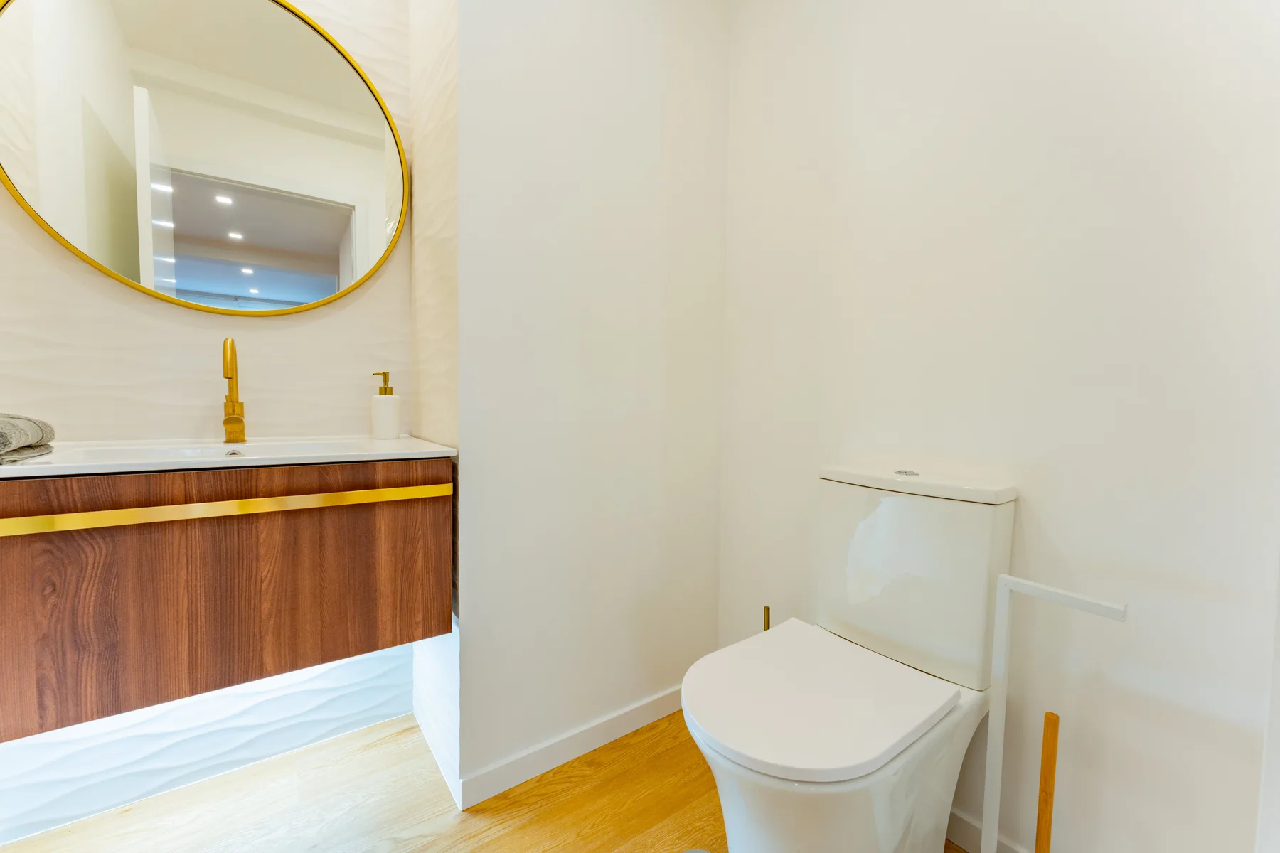 A bathroom with a toilet beside a vanity and round mirror.