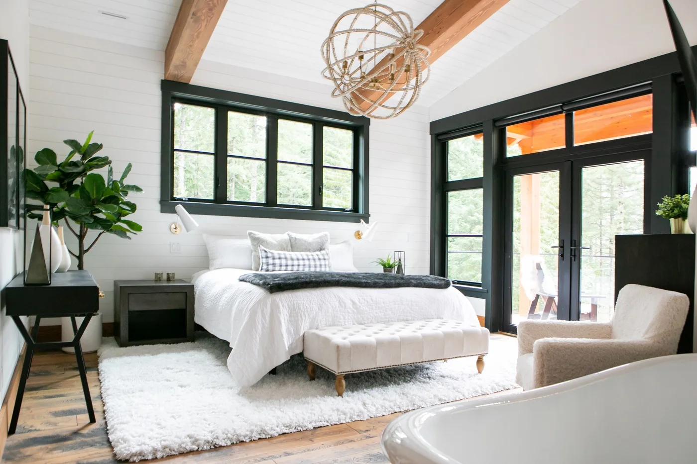 Un dormitorio luminoso con una cama blanca, ventanas grandes y puertas de vidrio.