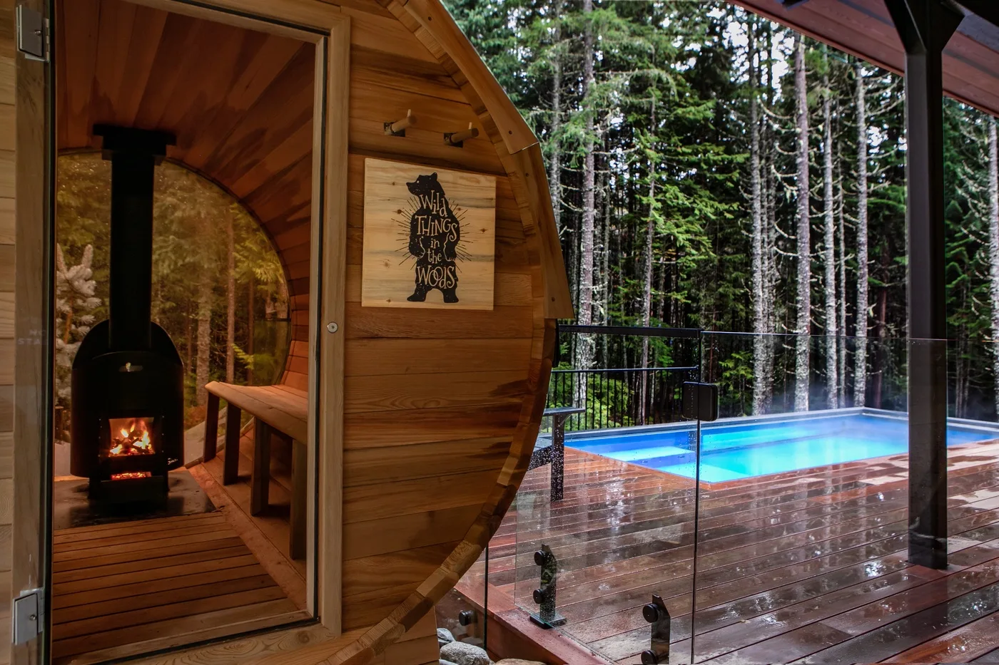 Una cabaña de madera con una estufa encendida da a una terraza junto a una piscina.