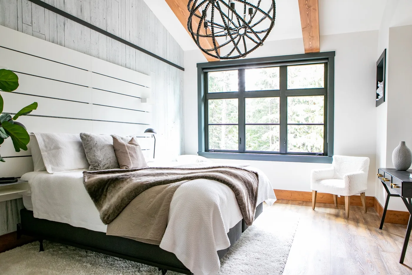 Un dormitorio luminoso con una cama grande, ventanas amplias y una zona de asiento blanca.