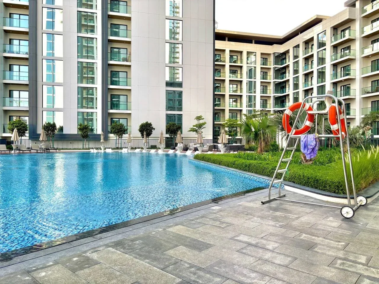 Una piscina al aire libre junto a una terraza pavimentada y edificios modernos.