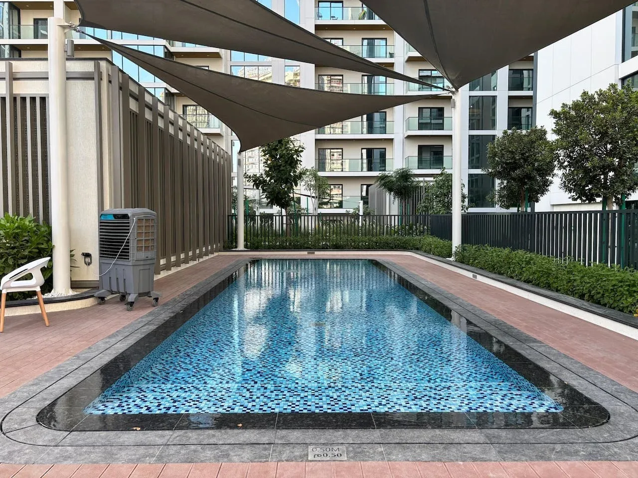 Una piscina en un patio está bajo toldos de sombra junto a edificios de apartamentos modernos.