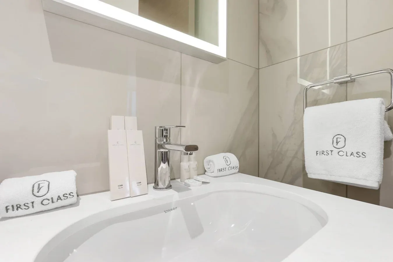Un tocador de baño con un lavabo blanco amplio, artículos de aseo y toallas dobladas.