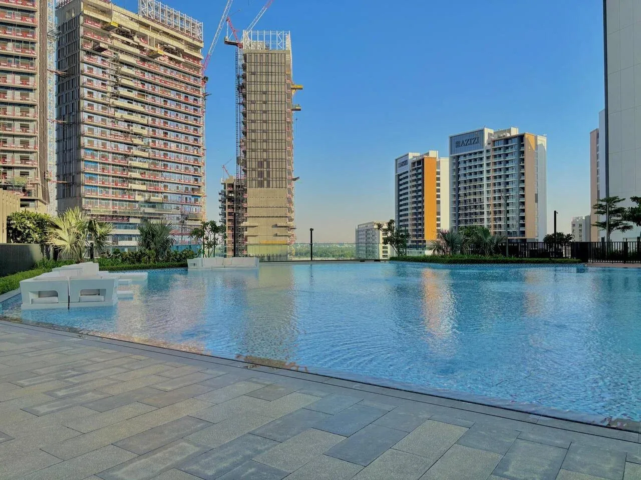 Una piscina junto a zonas pavimentadas para sentarse, con edificios altos al fondo.