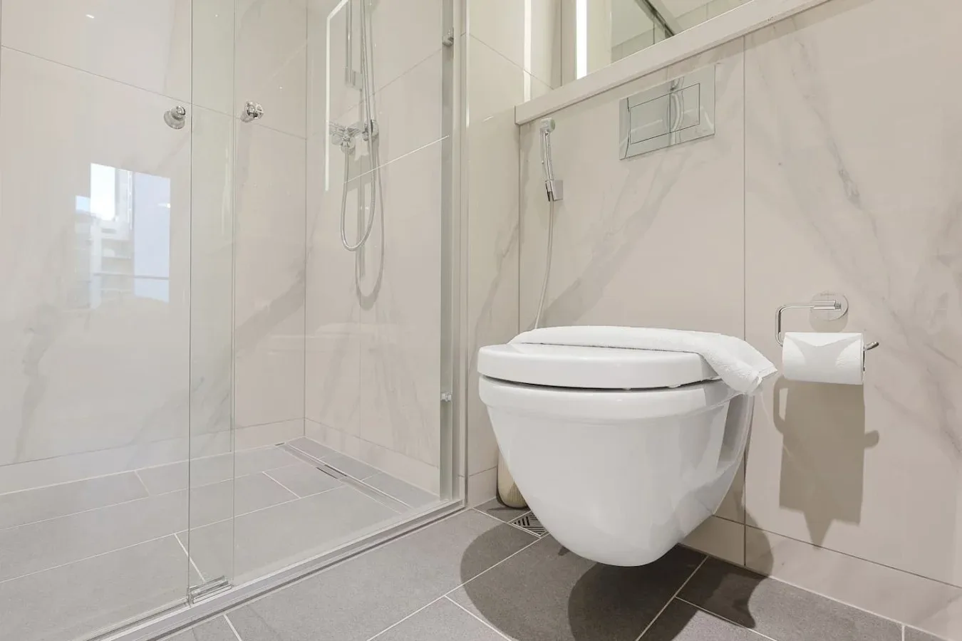 Un baño luminoso con ducha de vidrio y un inodoro suspendido.