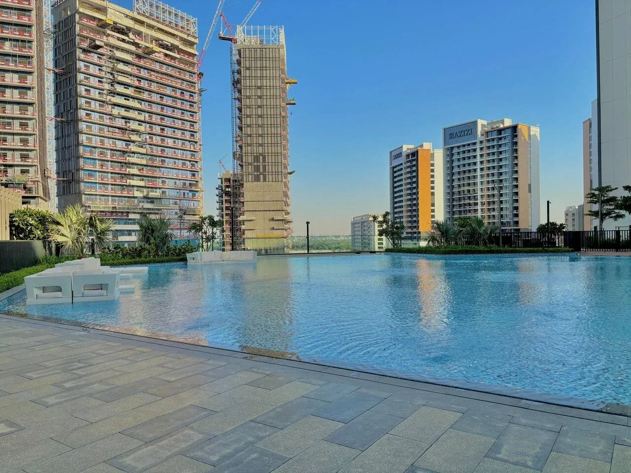 Una piscina se encuentra junto a edificios altos bajo un cielo azul despejado.