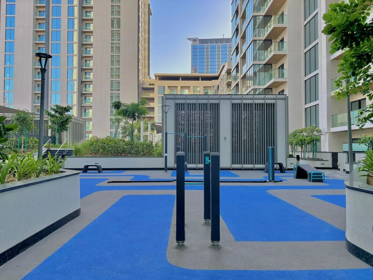 Una zona de ejercicio al aire libre con suelo azul y equipos entre edificios de apartamentos.