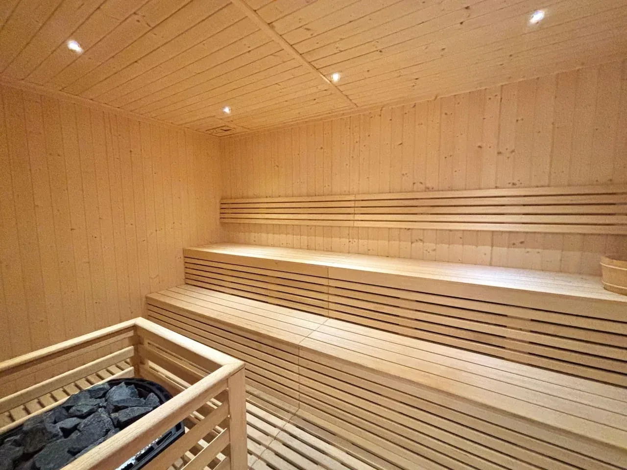 Una sauna revestida de madera con bancos escalonados y un calentador de piedras.