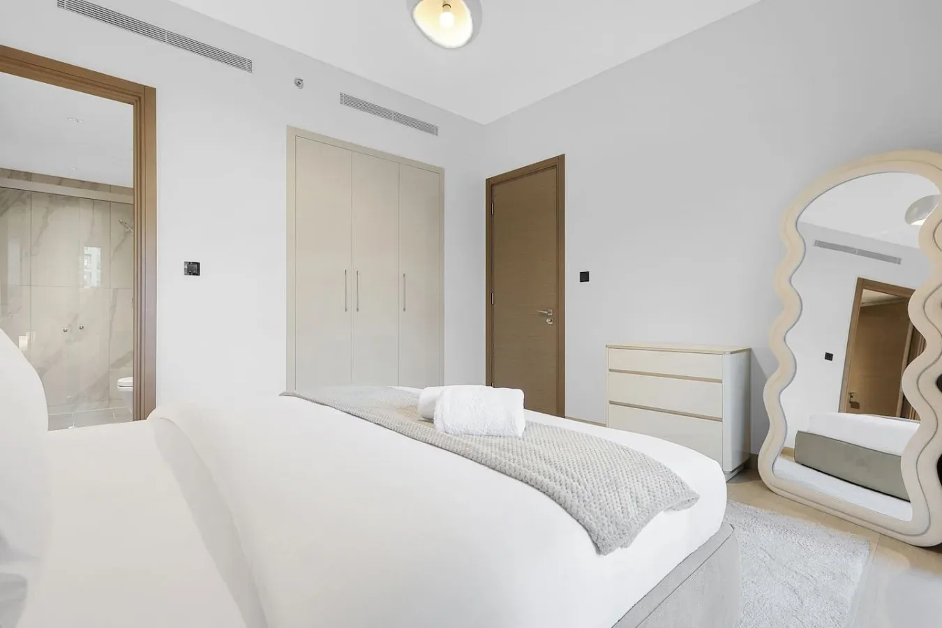 Un dormitorio luminoso con una cama bien arreglada y un espejo de cuerpo entero.