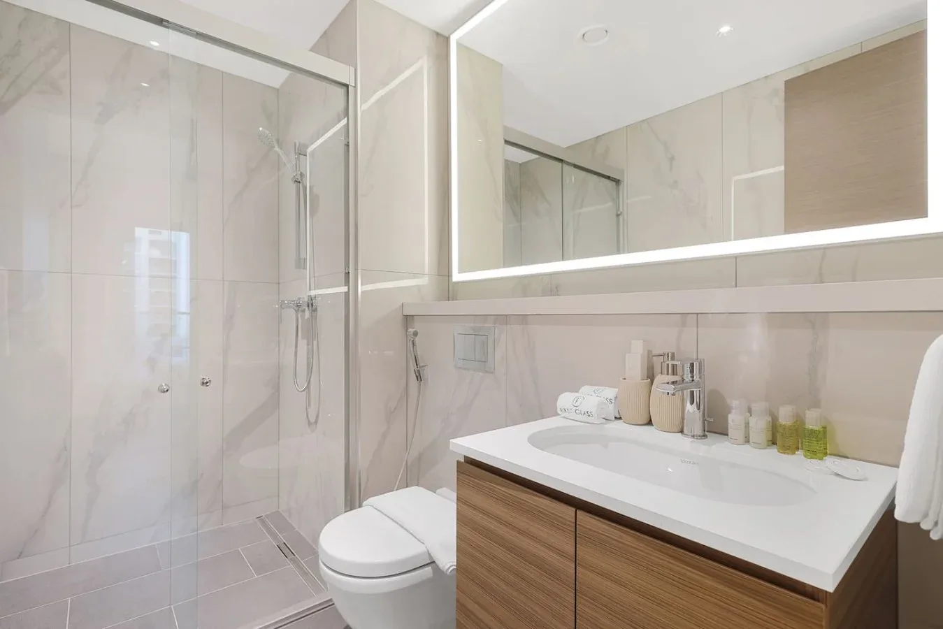 Un baño luminoso con ducha de vidrio y un lavabo bajo un espejo amplio.