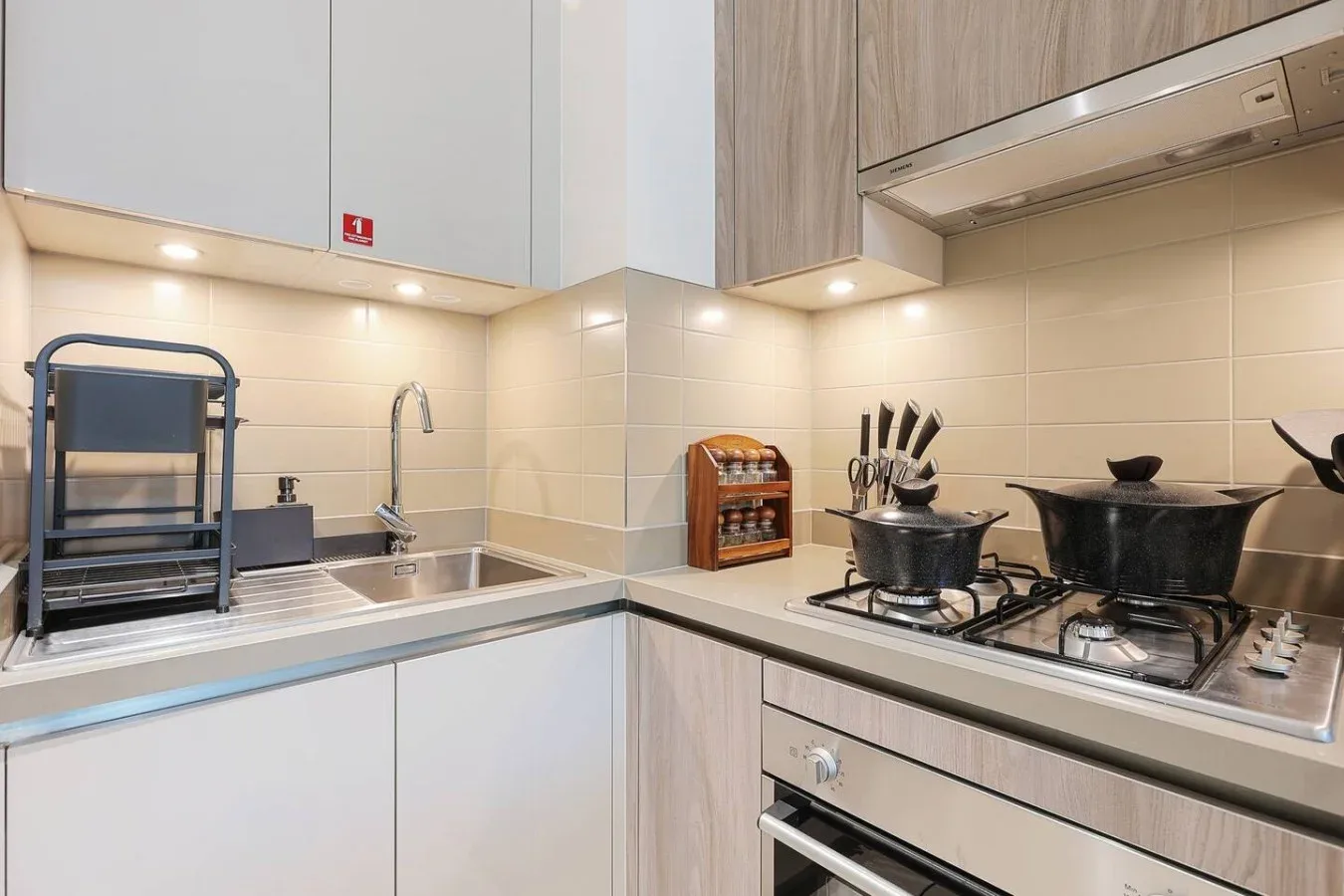 Una cocina moderna con fregadero y estufa de gas bajo armarios de madera clara.