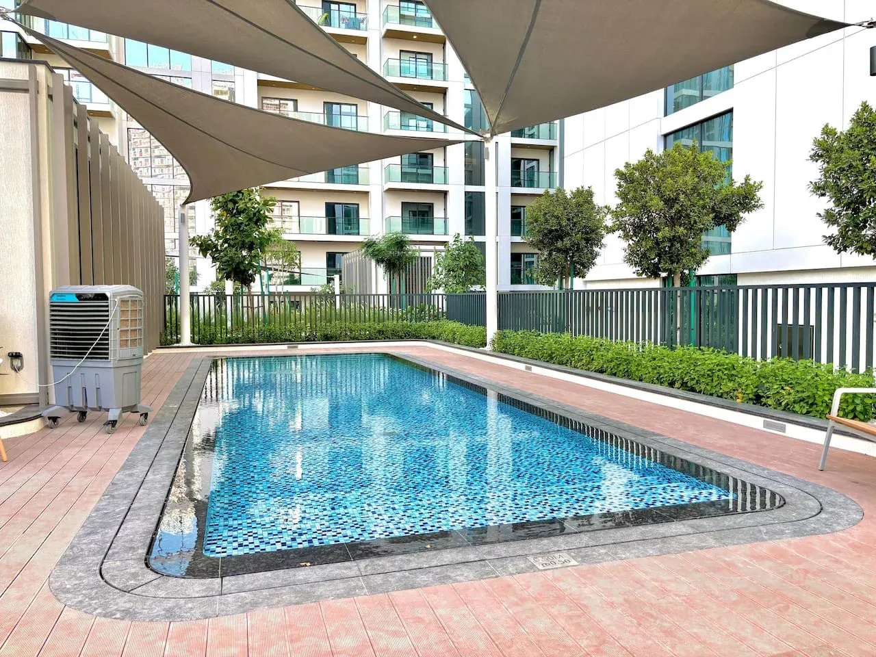 Una piscina al aire libre está rodeada de suelo embaldosado y toldos de sombra.