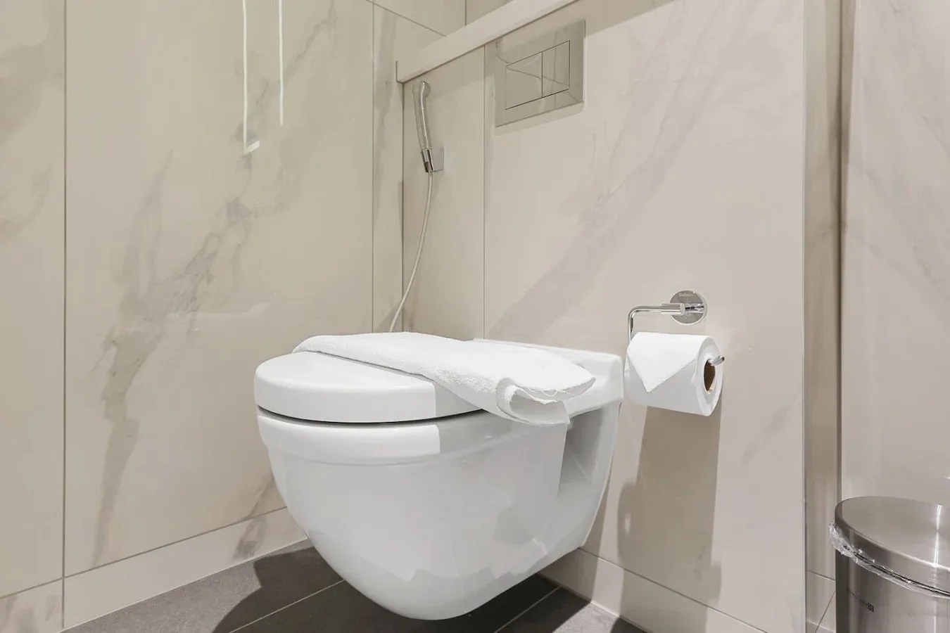 Un baño moderno con un inodoro suspendido y paredes de azulejos claros.