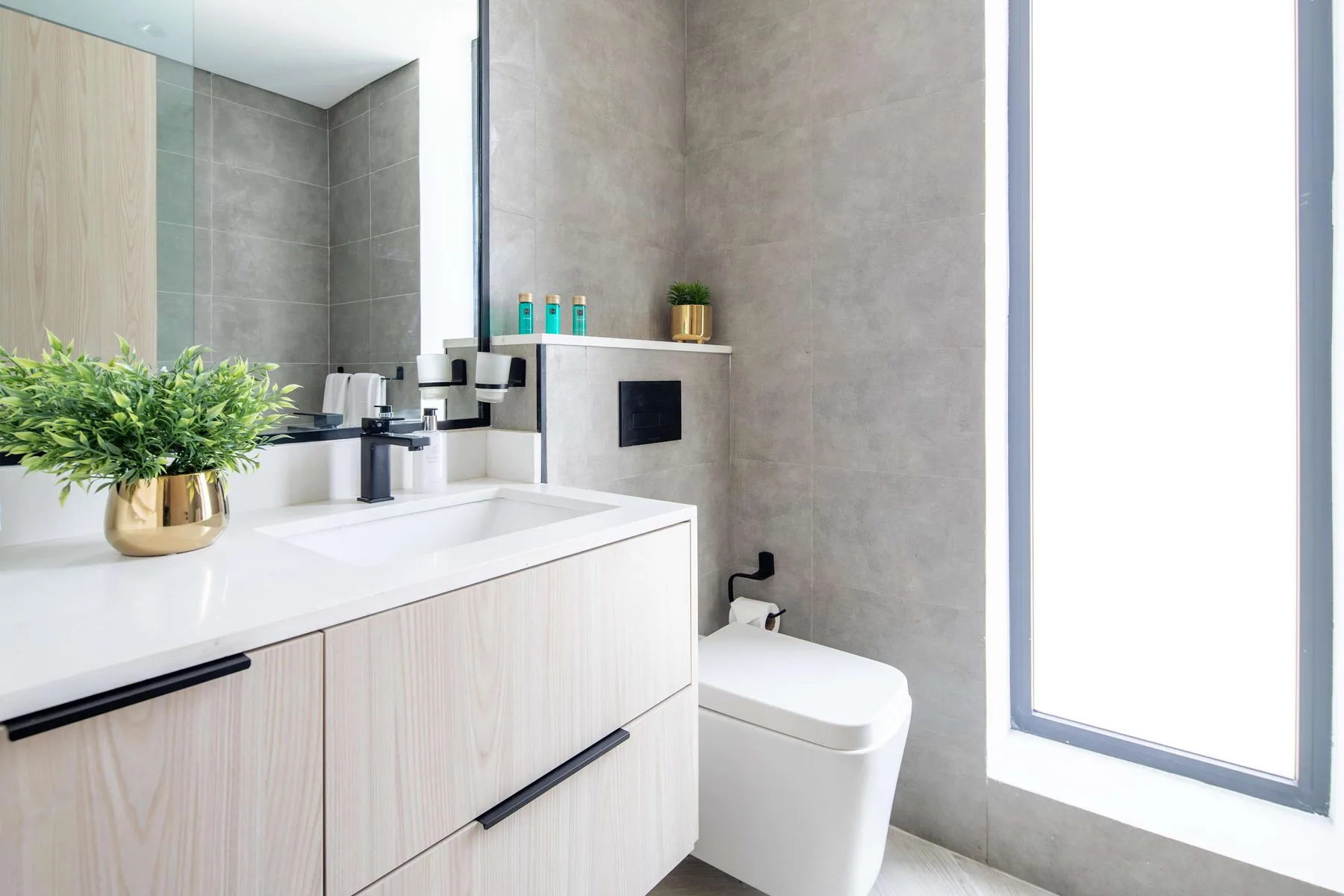 A modern bathroom vanity with a sink and toilet beside a bright window.
