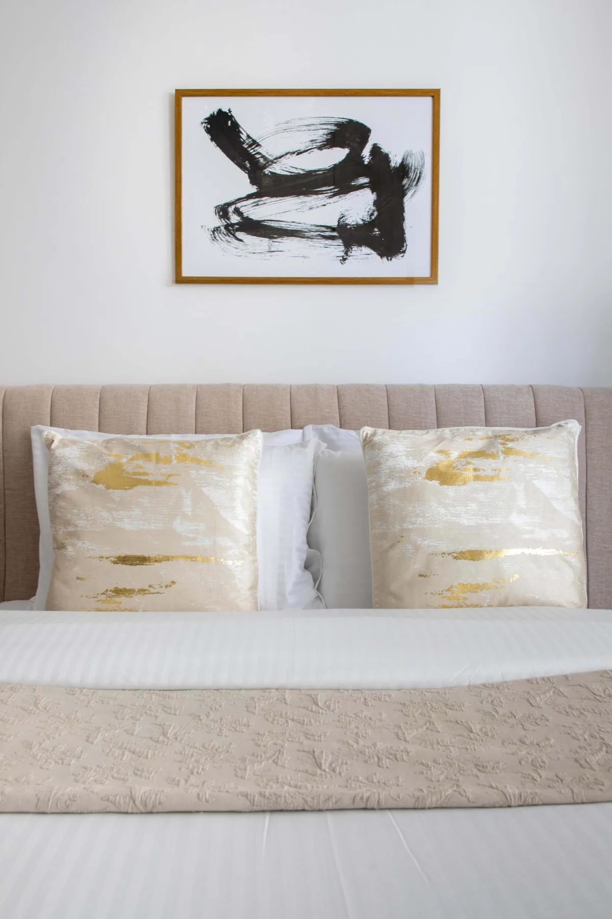 A neatly made bed with decorative pillows sits beneath framed abstract artwork.