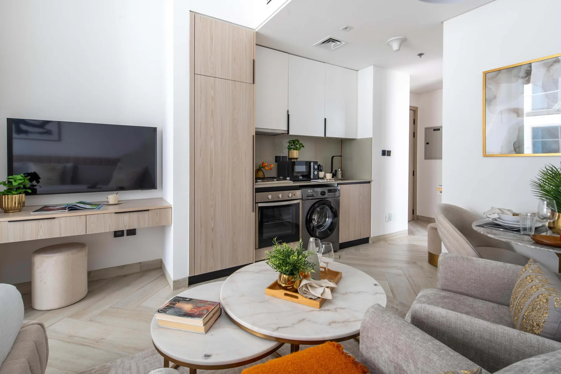 A bright living room with a seating area, television, and compact kitchen.
