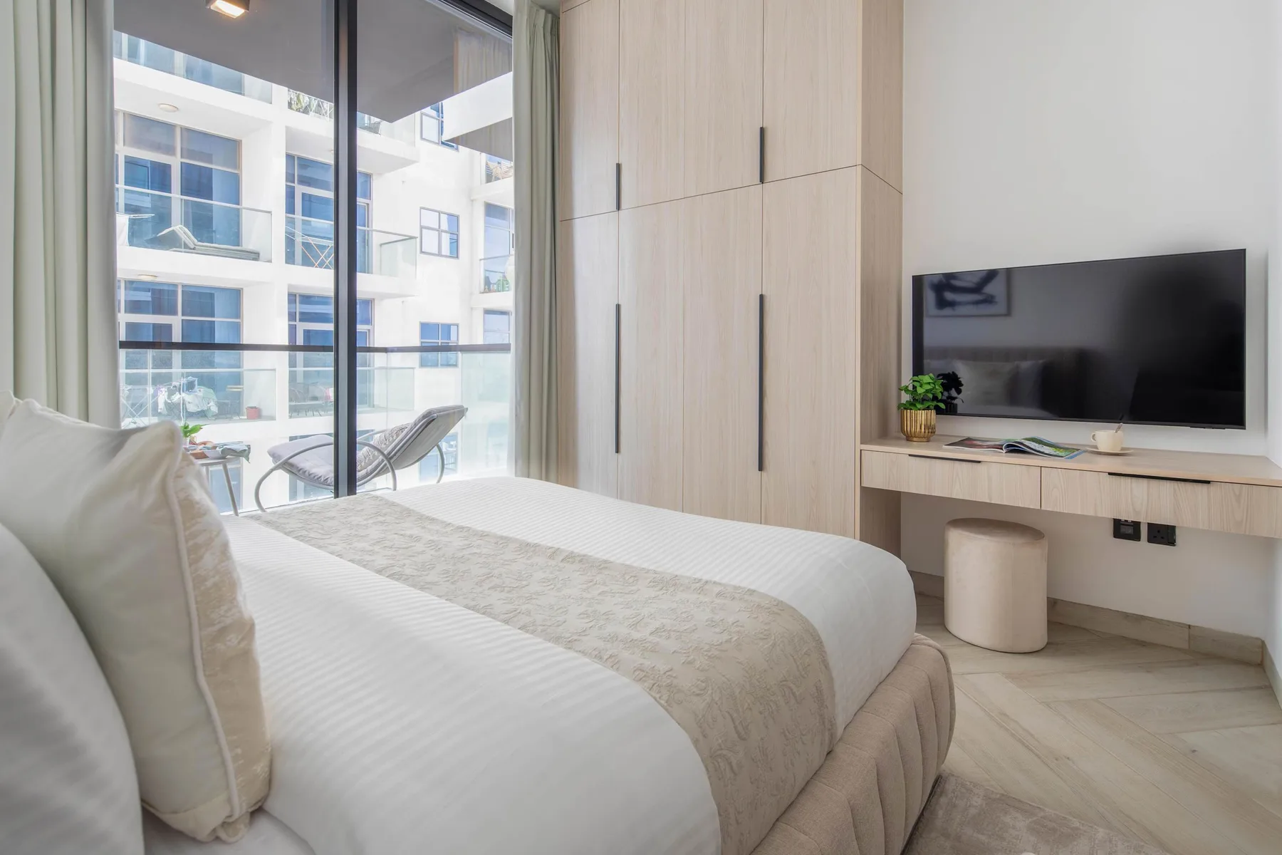 A bright bedroom with a bed beside a large window and a television.