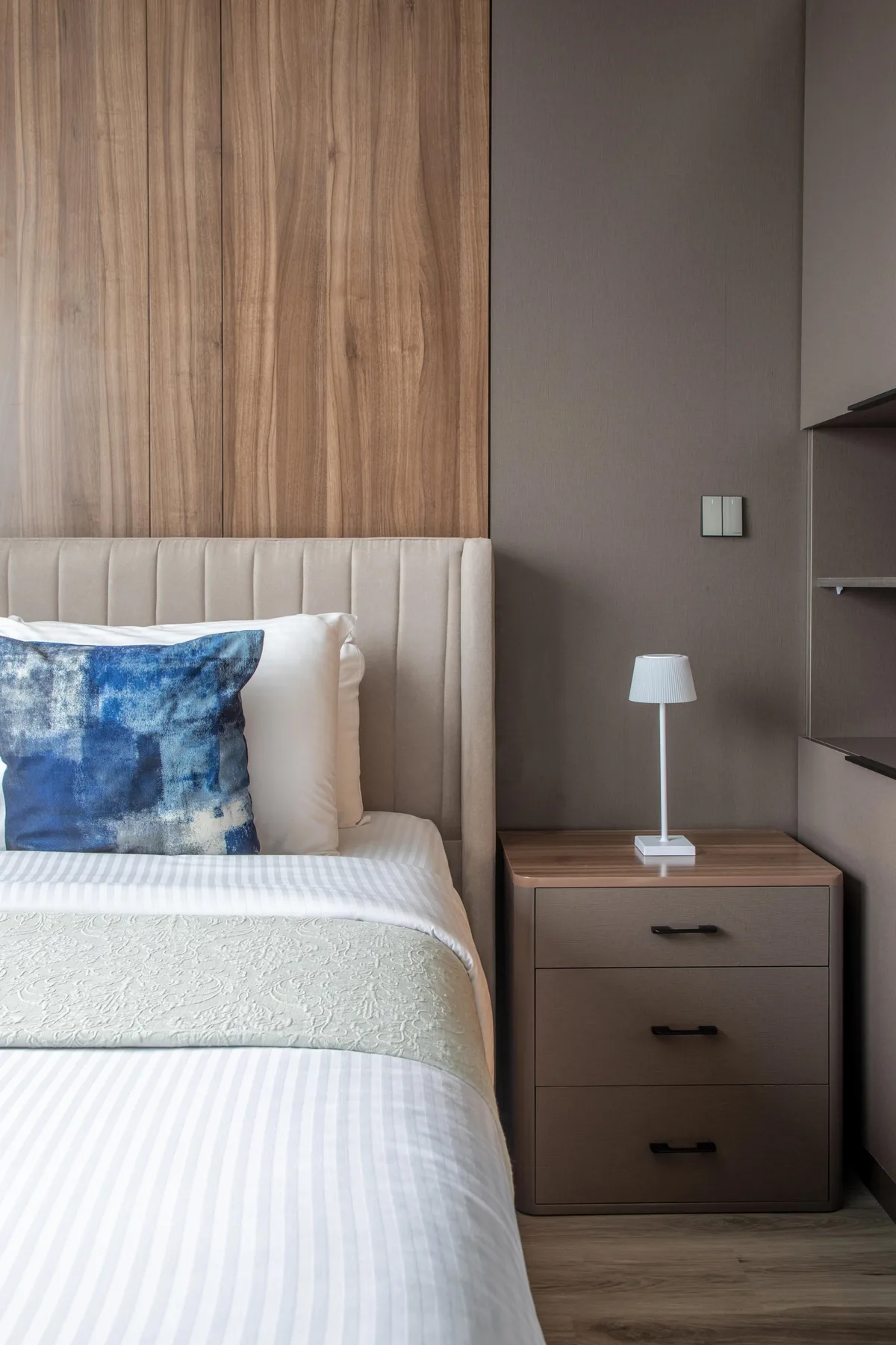 Un dormitorio con una cama bien tendida, una mesita de noche y una lámpara pequeña.