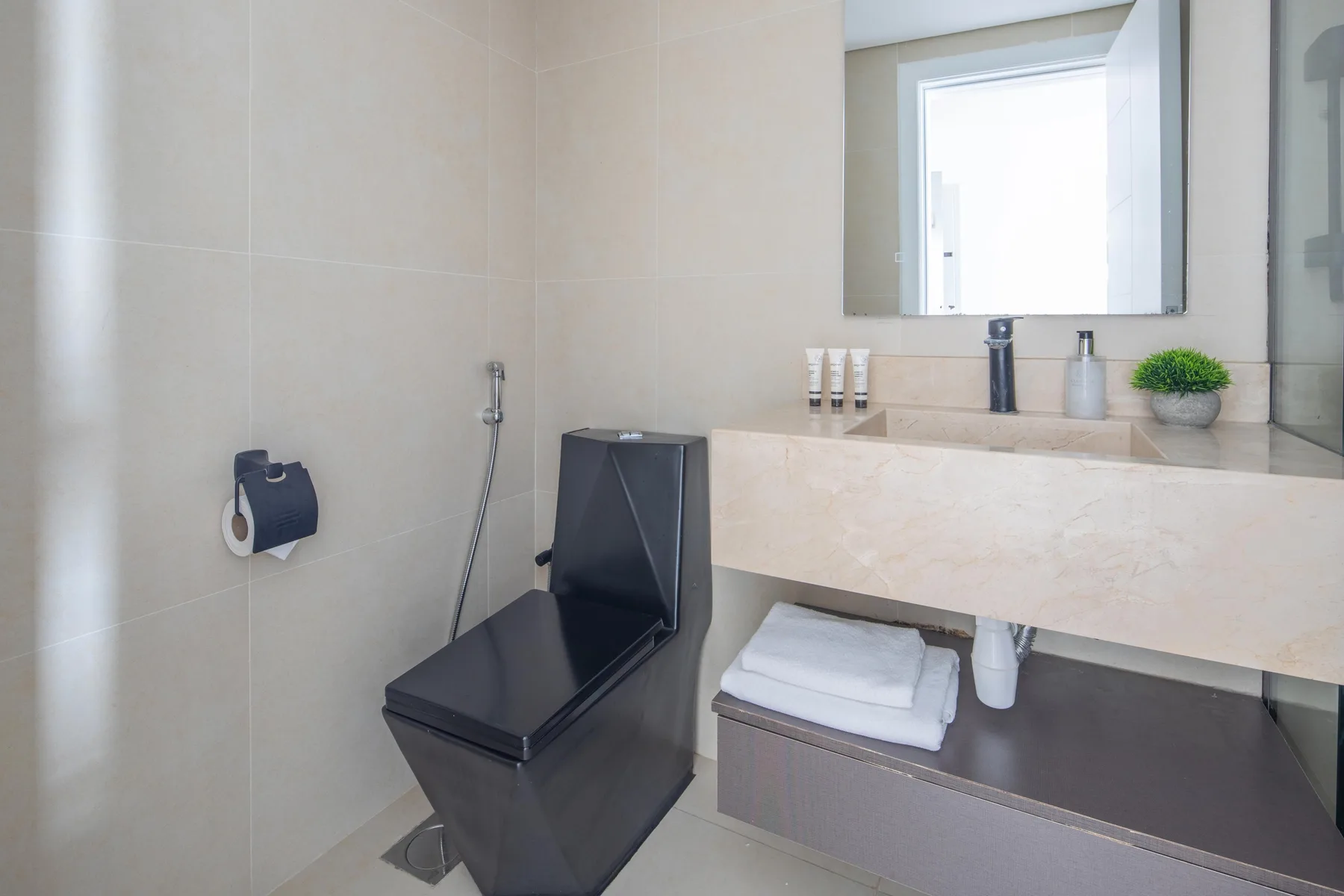 Un baño moderno con un inodoro oscuro, paredes de azulejos claros y un amplio tocador.